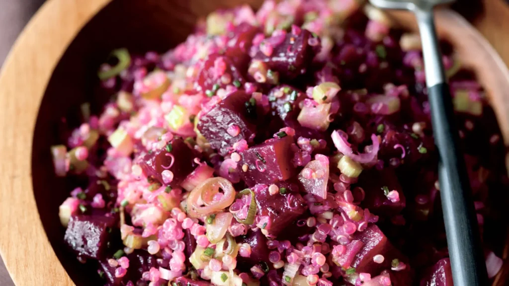 Grosse cuillerée de salade composée de betterave en dés, quinoa, céleri et échalotes dans un bol en bois avec une cuillère noire.