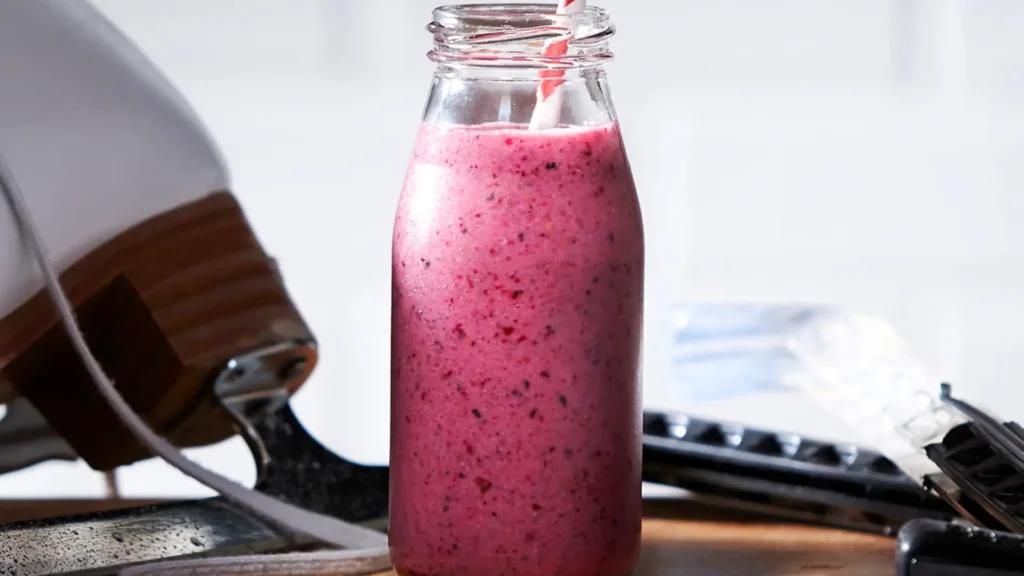 Recettes betterave: Bouteille en verre remplie de smoothie rose aux fruits rouges avec une paille rayée rouge et blanche, posée devant une paire de patins à glace.