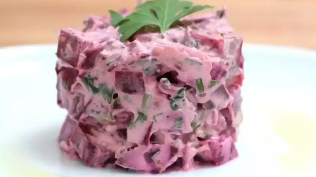 recettes alcalines betterave: Tartare de betterave crémeux, moulé en cylindre et garni d’une feuille de persil, présenté sur une assiette blanche.