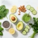 Flat lay d'aliments alcalins : épinards, avocat, citron, concombre, amandes, graines de chia et smoothie vert sur marbre blanc