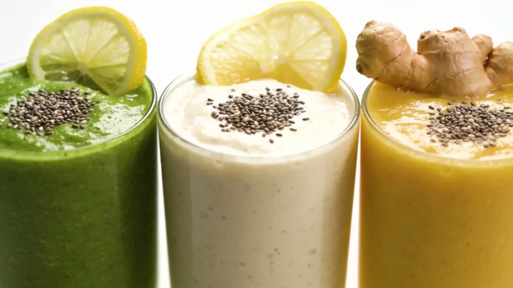 Trois verres de smoothie alcalin alignés sur fond blanc : smoothie vert au citron vert, smoothie crémeux banane au citron et smoothie doré au gingembre, tous garnis de graines de chia