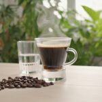 Café acide ou alcalin ? 7 réponses claires pour votre pH 17 Café acide ou alcalin : Tasse de café filtre fumante entourée de grains de café et d'un verre d'eau sur une table claire