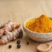 Rhizomes de curcuma frais et bol de poudre de curcuma orange avec des grains de poivre noir