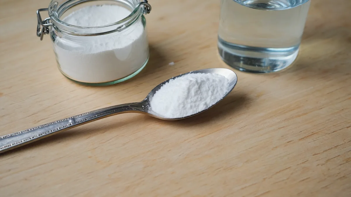 Bicarbonate de soude : 6 bienfaits et le verdict définitif 5 Cuillère bombée de bicarbonate de soude devant un bocal en verre et un verre d'eau