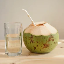 Eau de coco servie dans un verre à côté d'une noix de coco verte ouverte