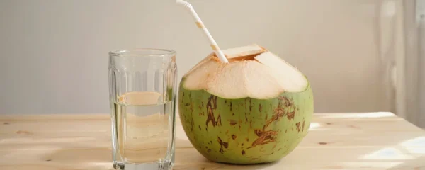 Eau de coco servie dans un verre à côté d'une noix de coco verte ouverte