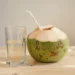 Eau de coco servie dans un verre à côté d'une noix de coco verte ouverte