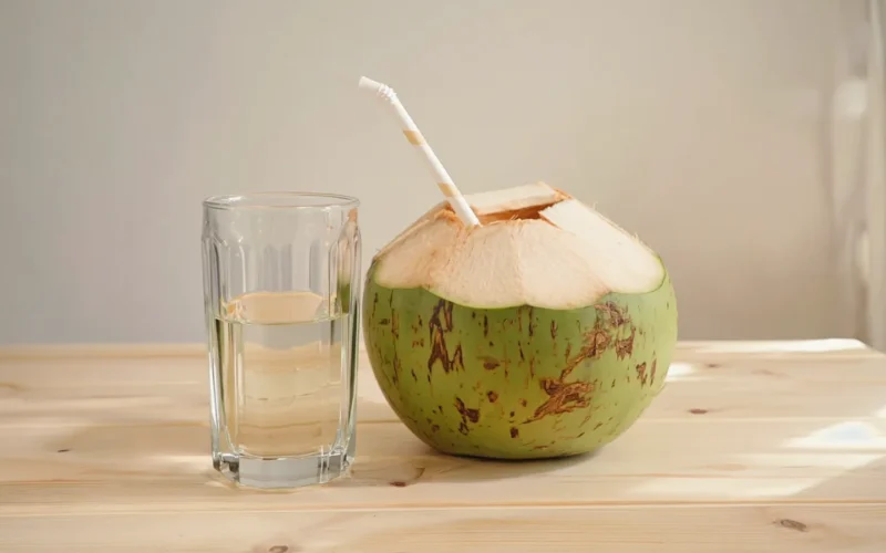 Eau de coco : 5 bienfaits réels et le comparatif essentiel 1 Eau de coco servie dans un verre à côté d'une noix de coco verte ouverte