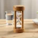Jeûne intermittent : sablier en bois, verre d'eau et tasse de thé sur une table claire